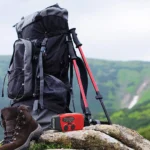 Emergency Weather Radio — Hand Crank & Solar with Flashlight and USB Phone Charger — packed beside a hiking backpack on a mountain trail